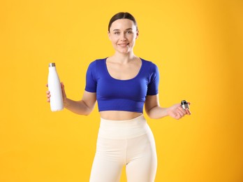 Woman in stylish sportswear with water bottle on orange background