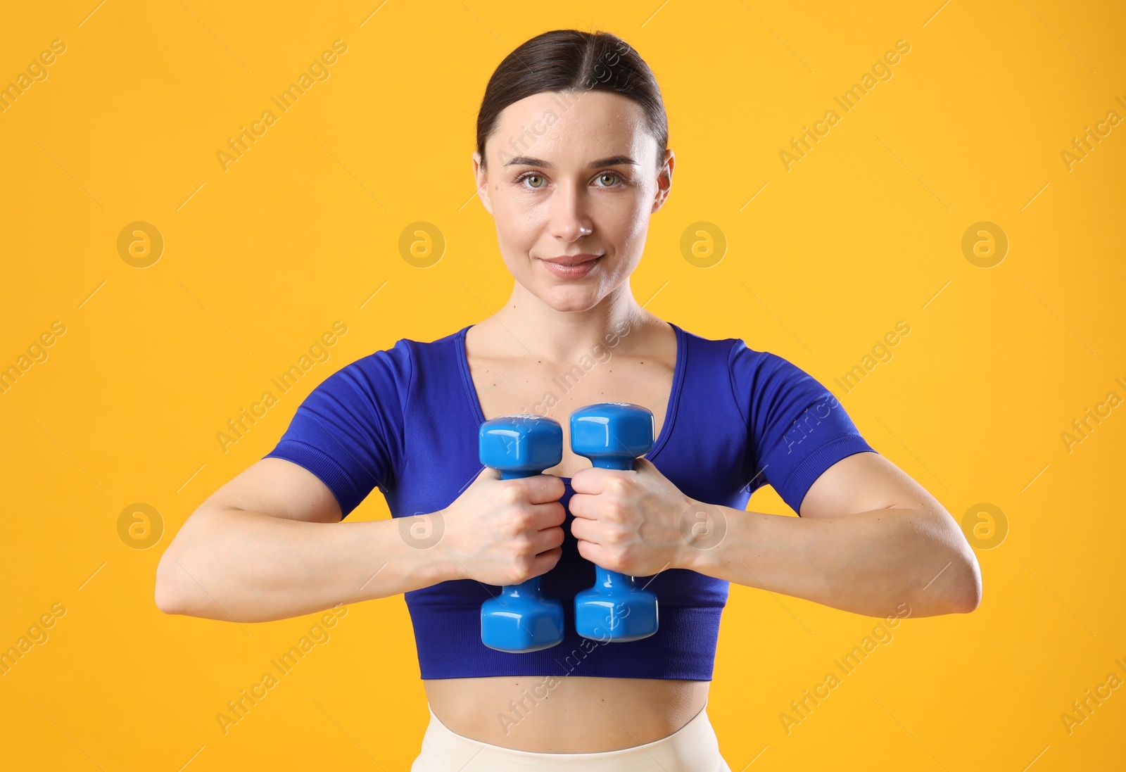 Photo of Woman in sportswear exercising with dumbbells on orange background