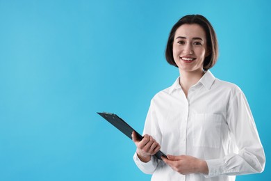 Portrait of young secretary with clipboard on light blue background. Space for text