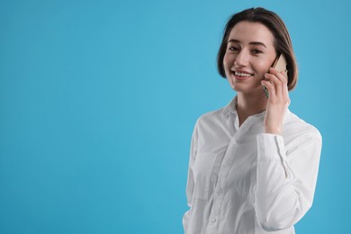 Smiling secretary talking on smartphone against light blue background. Space for text