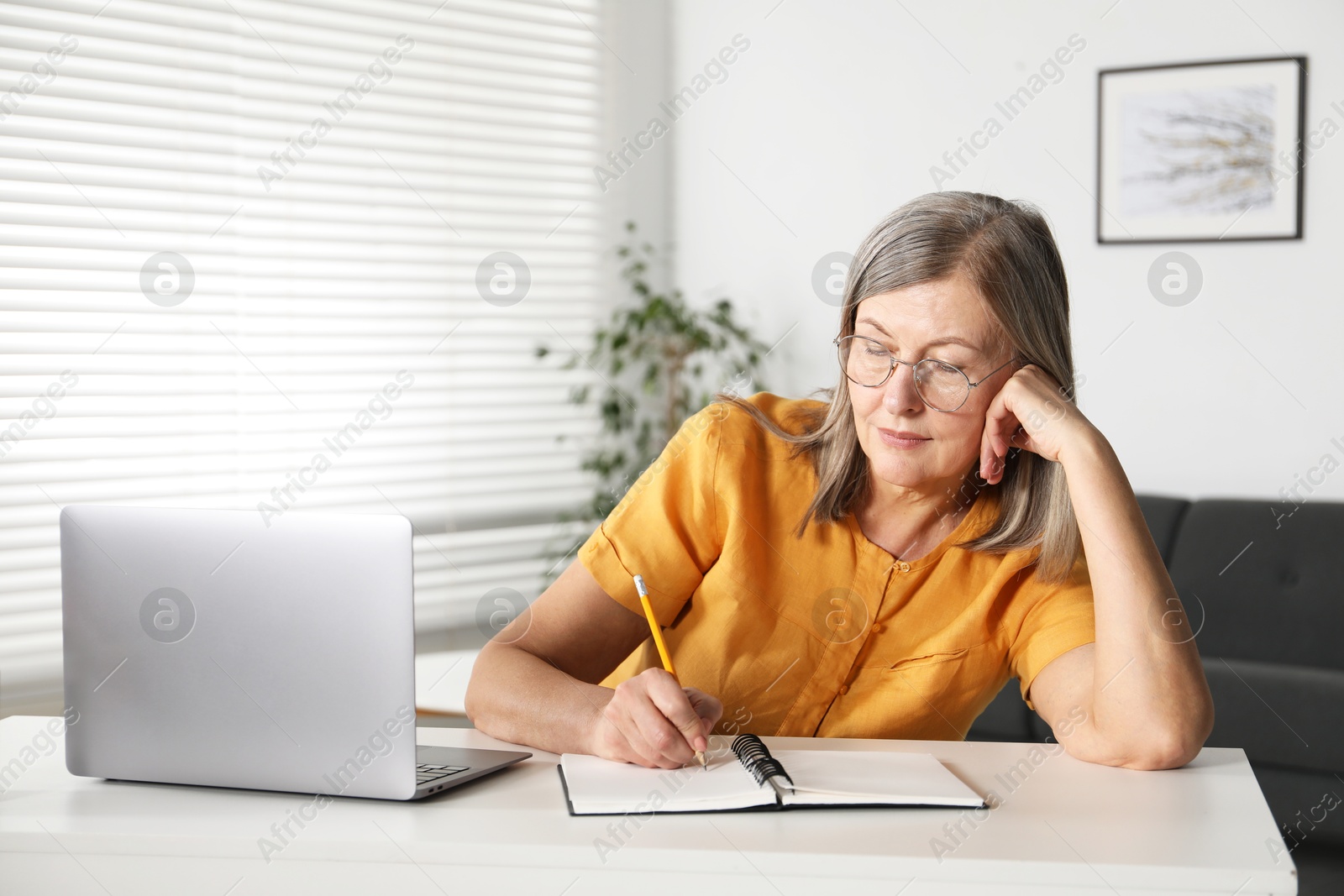 Photo of Woman learning online using laptop and taking notes at table indoors. Self-study