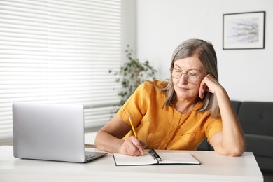 Photo of Woman learning online using laptop and taking notes at table indoors. Self-study