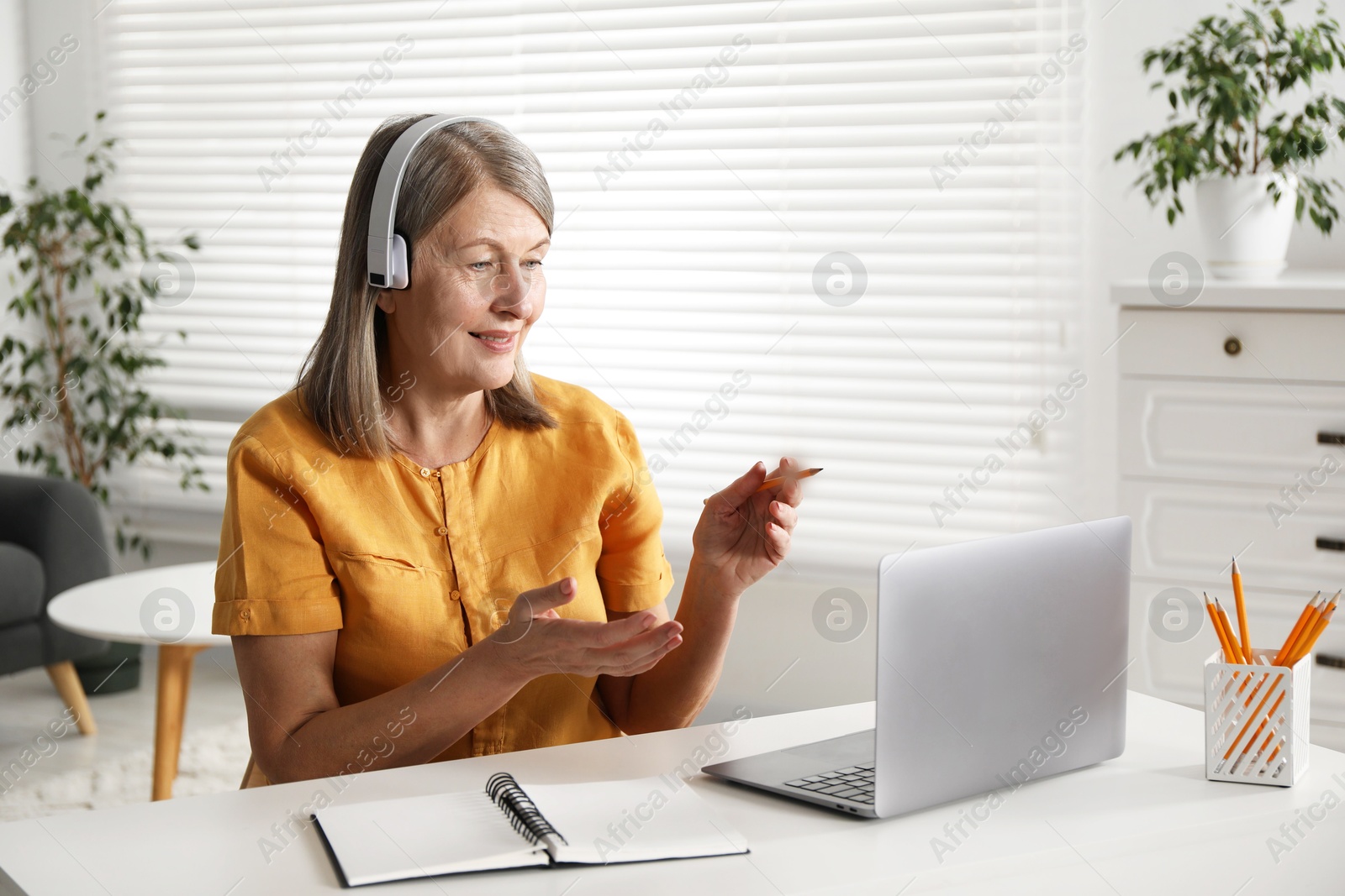 Photo of Smiling woman having online lesson with teacher by laptop at table indoors