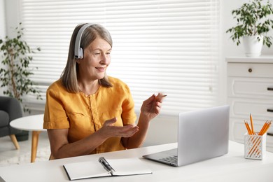 Smiling woman having online lesson with teacher by laptop at table indoors