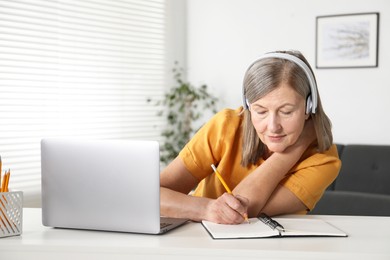 Photo of Woman learning online using laptop and taking notes at table indoors. Self-study