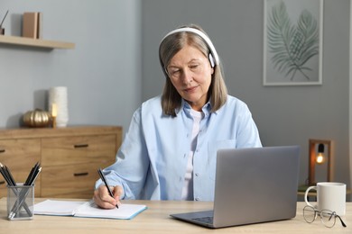 Photo of Woman learning online using laptop and taking notes at table indoors. Self-study