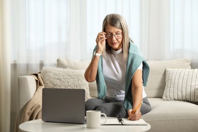 Photo of Woman learning online using laptop and taking notes at table indoors. Self-study