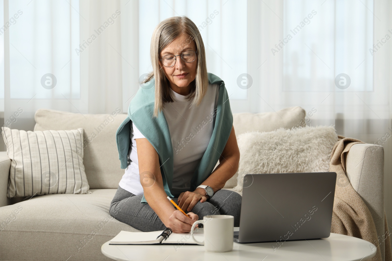 Photo of Woman learning online using laptop and taking notes at table indoors. Self-study