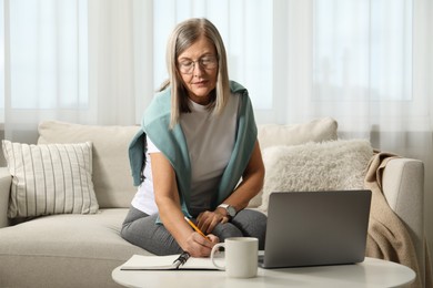 Woman learning online using laptop and taking notes at table indoors. Self-study