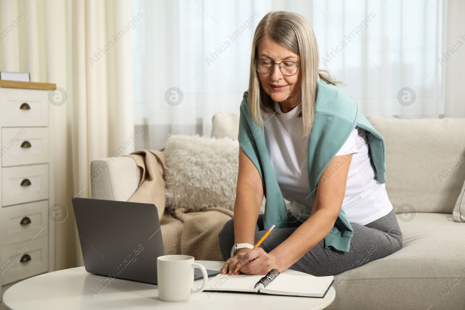 Photo of Woman learning online using laptop and taking notes at table indoors. Self-study