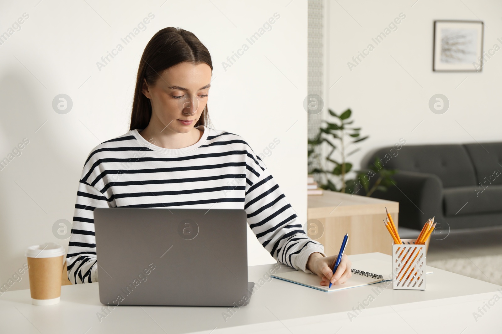 Photo of Woman taking notes during online lesson at table indoors. Self-study