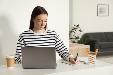 Woman taking notes during online lesson at table indoors. Self-study