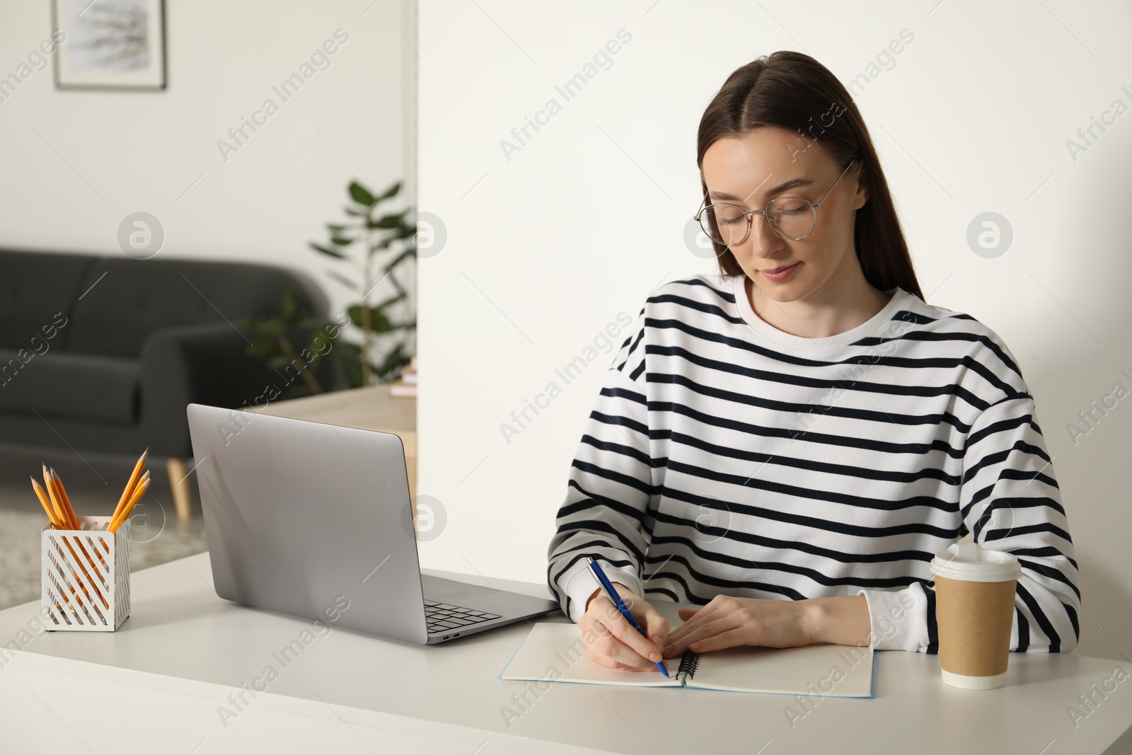 Photo of Woman taking notes during online lesson at table indoors. Self-study