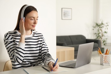 Woman taking notes during online lesson at table indoors. Self-study