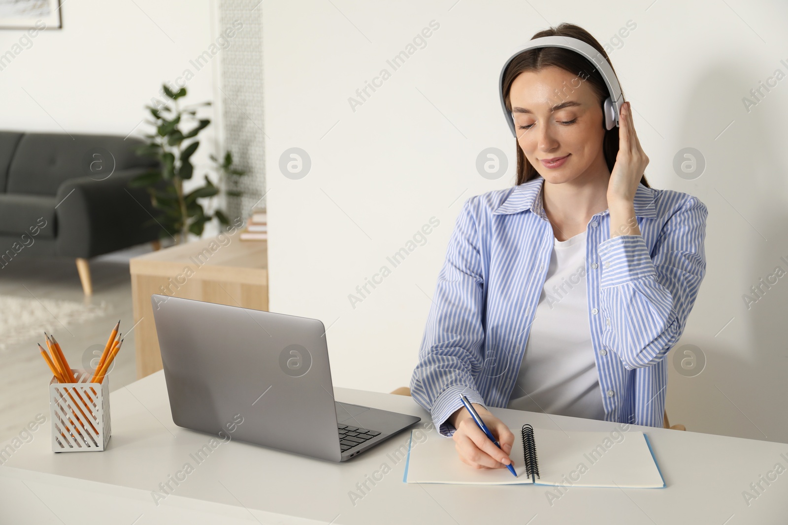 Photo of Woman taking notes during online lesson at table indoors. Self-study