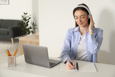 Woman taking notes during online lesson at table indoors. Self-study