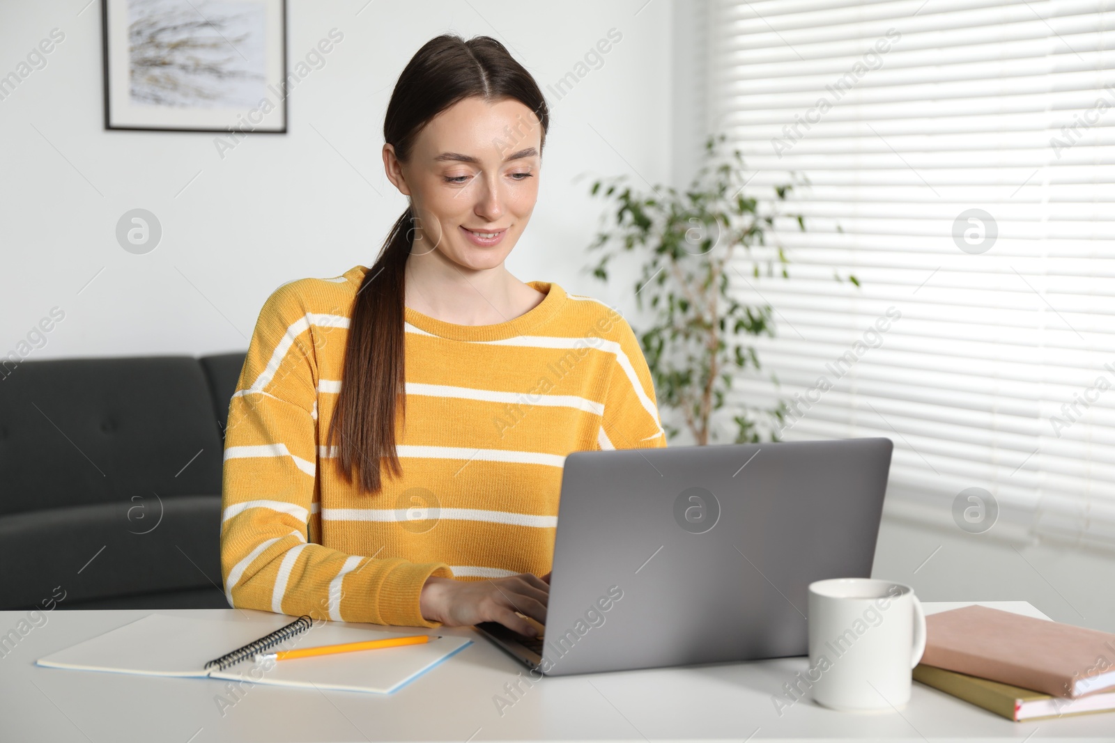 Photo of Smiling woman learning online using laptop at table indoors. Self-study