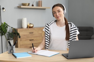 Woman taking notes during online lesson at table indoors. Self-study