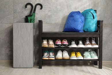 Photo of Shoe storage bench with different footwear, backpack, sport's bag and umbrellas indoors