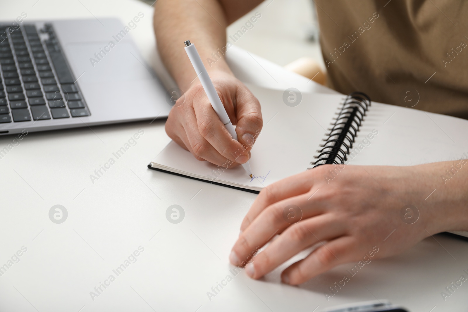 Photo of Man taking notes during online lesson at desk indoors, closeup. Self-study