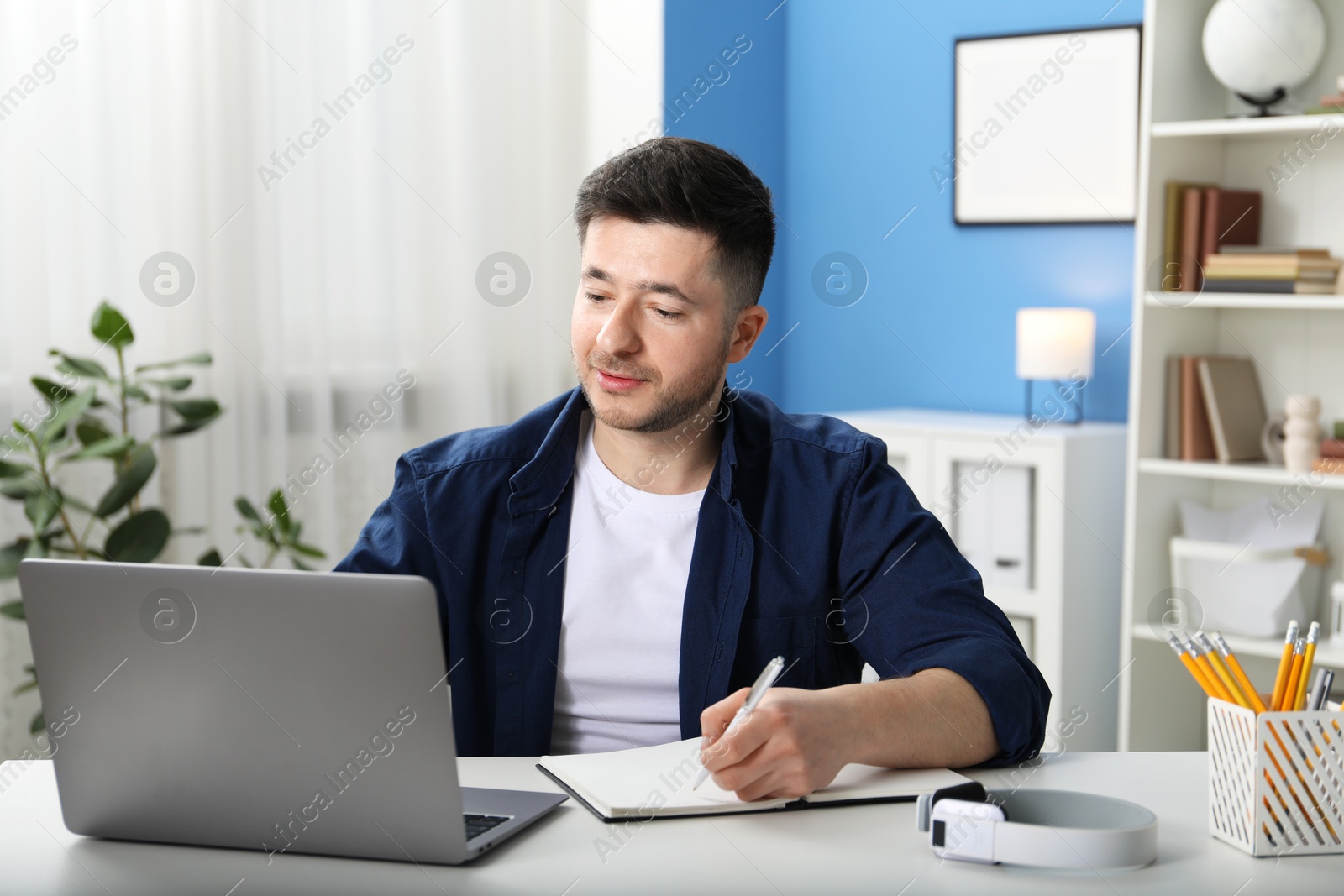 Photo of Man taking notes during online lesson at desk indoors. Self-study