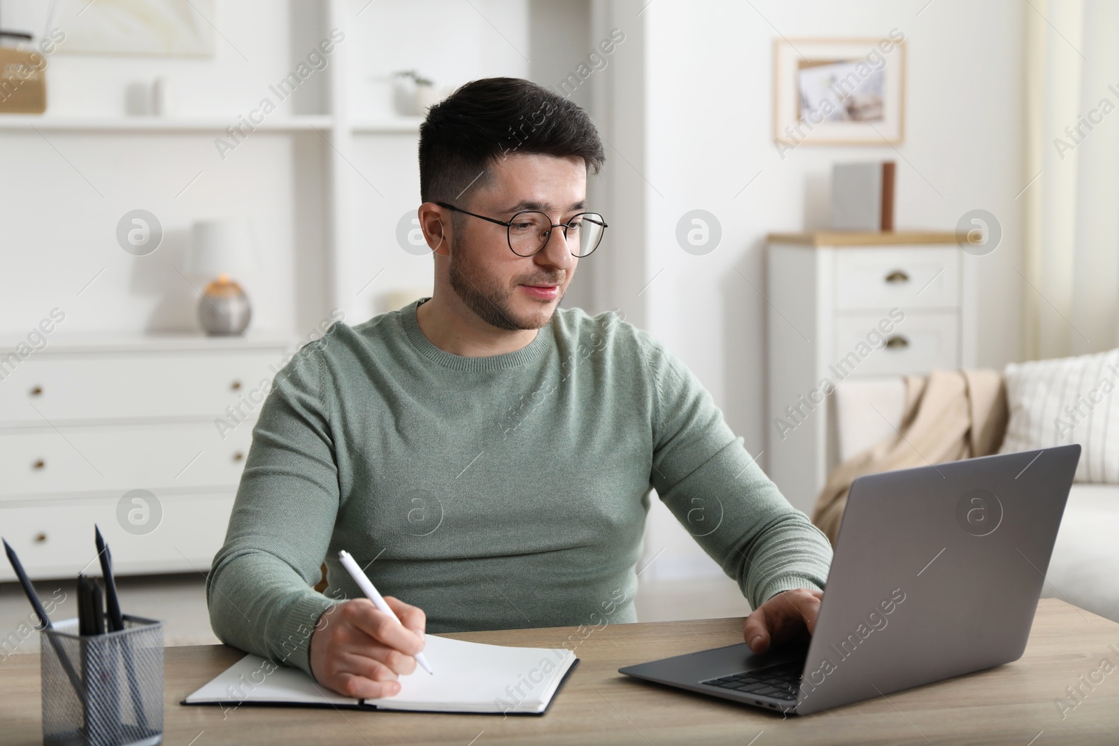 Photo of Man taking notes during online lesson at desk indoors. Self-study