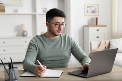 Photo of Man taking notes during online lesson at desk indoors. Self-study