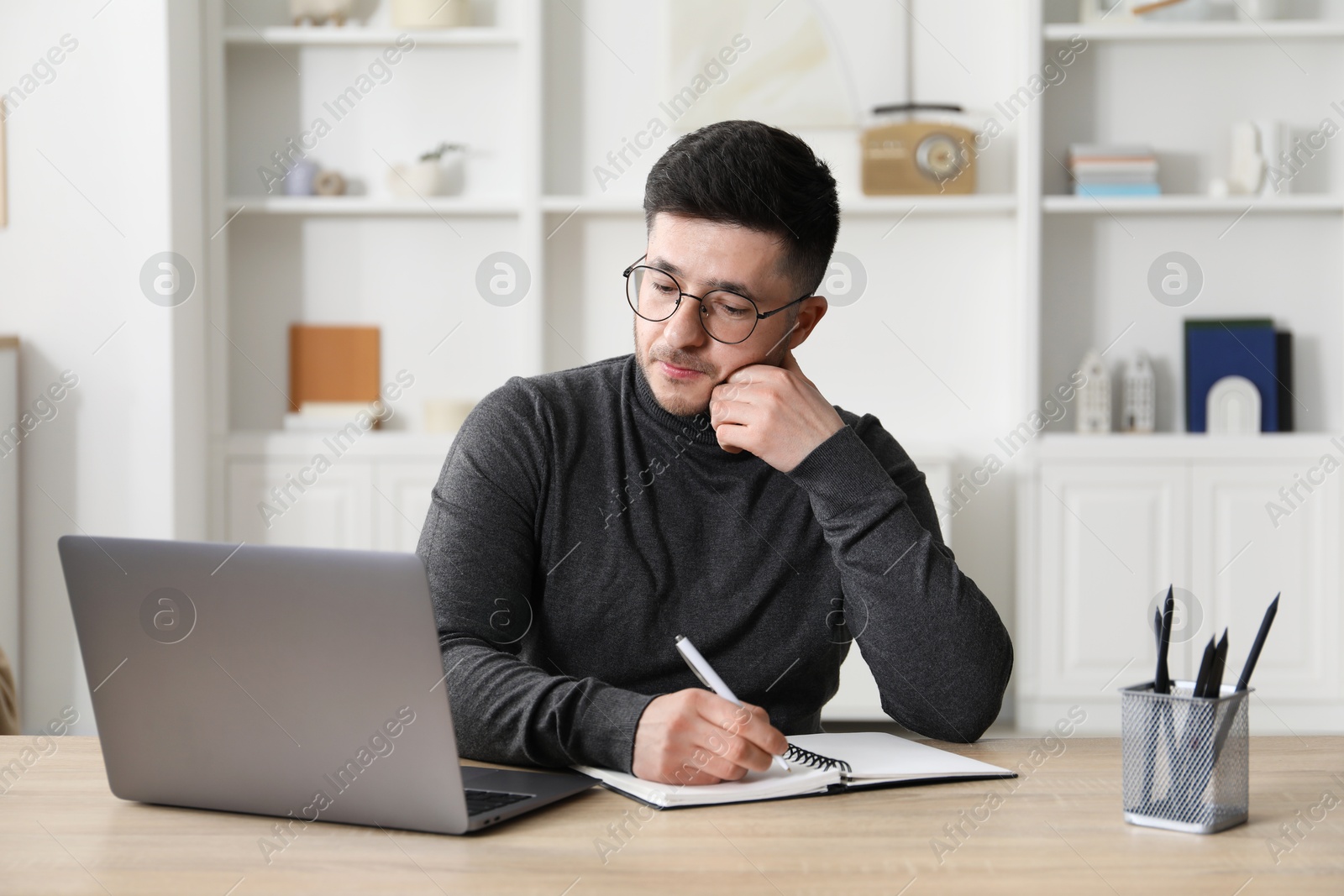 Photo of Man taking notes during online lesson at desk indoors. Self-study