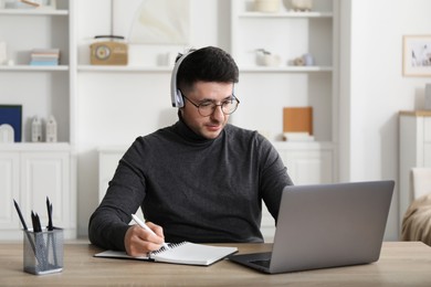 Photo of Man taking notes during online lesson at desk indoors. Self-study