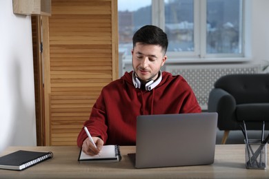 Photo of Man taking notes during online lesson at desk indoors. Self-study