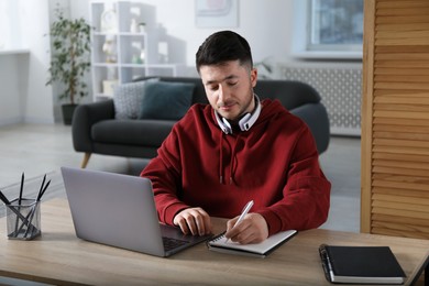 Photo of Man taking notes during online lesson at desk indoors. Self-study