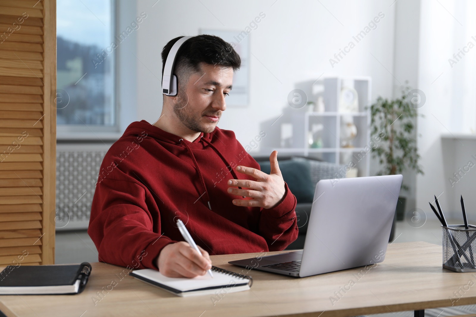 Photo of Man taking notes during online lesson with teacher at table indoors