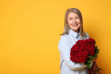 Smiling woman with bouquet of roses on yellow background. Space for text