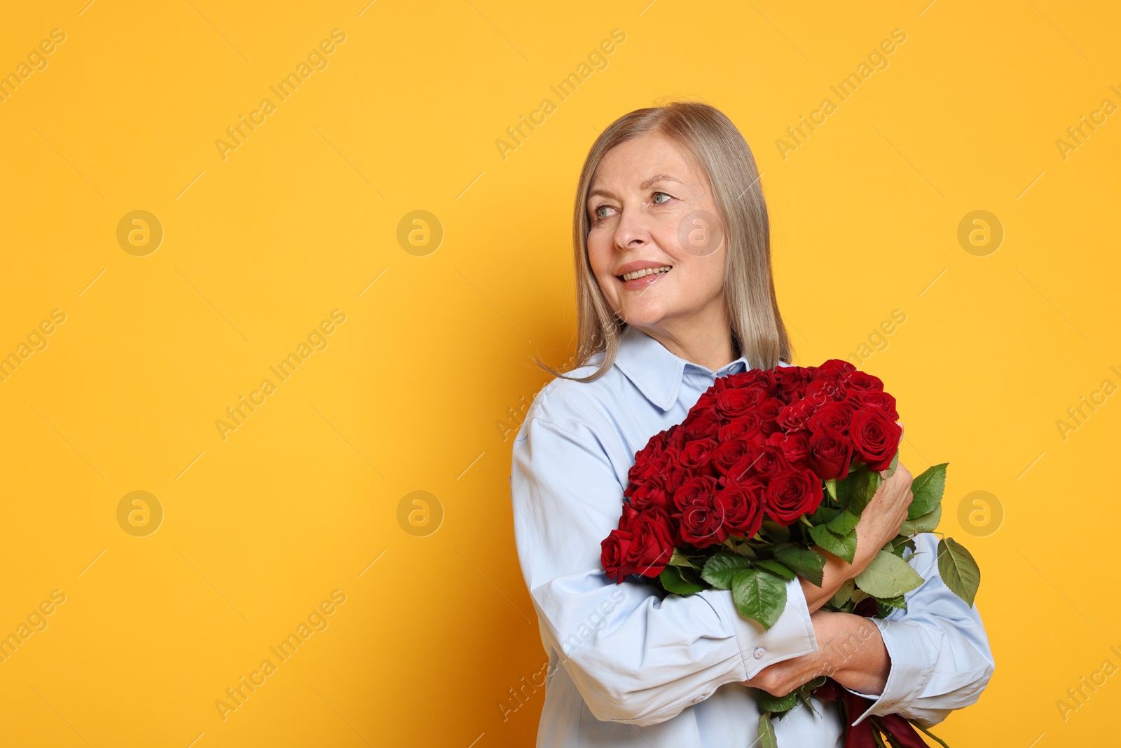 Photo of Smiling woman with bouquet of roses on yellow background. Space for text