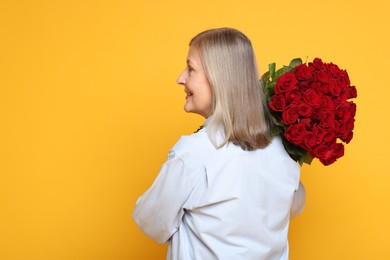 Photo of Smiling woman with bouquet of roses on yellow background, back view. Space for text