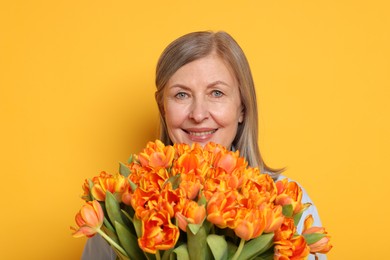 Smiling woman with bouquet of tulips on yellow background