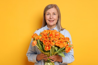 Smiling woman with bouquet of tulips on yellow background