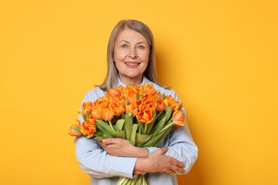 Smiling woman with bouquet of tulips on yellow background