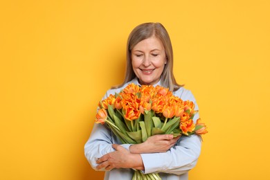 Photo of Smiling woman with bouquet of tulips on yellow background