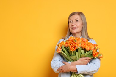 Photo of Smiling woman with bouquet of tulips on yellow background. Space for text