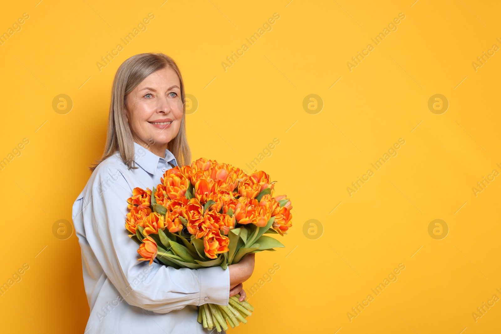 Photo of Smiling woman with bouquet of tulips on yellow background. Space for text