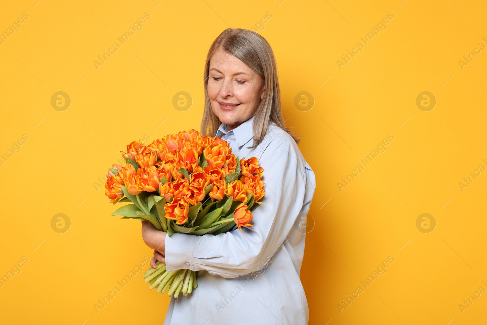 Photo of Smiling woman with bouquet of tulips on yellow background