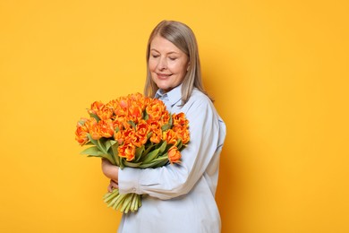 Smiling woman with bouquet of tulips on yellow background