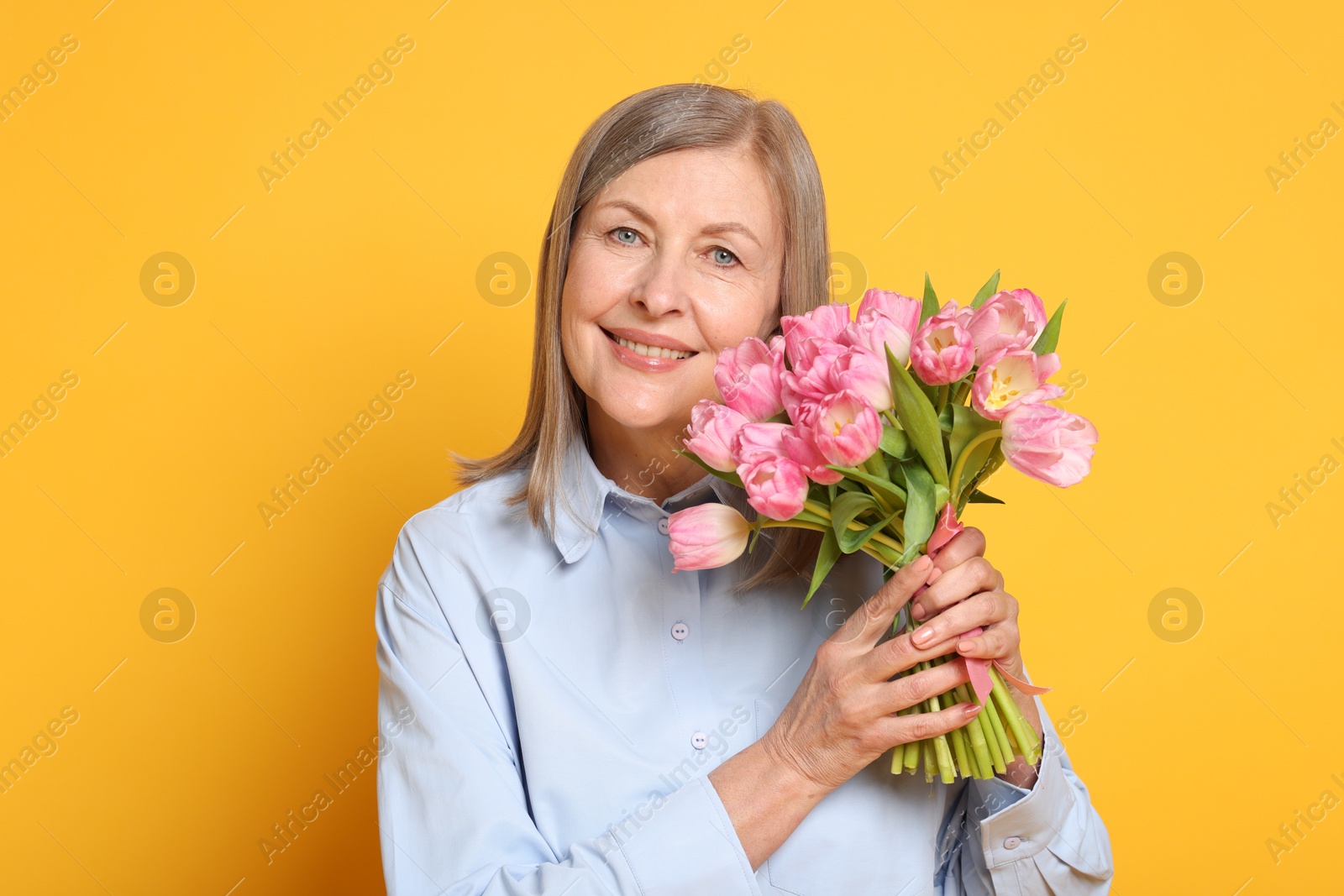 Photo of Smiling woman with bouquet of tulips on yellow background