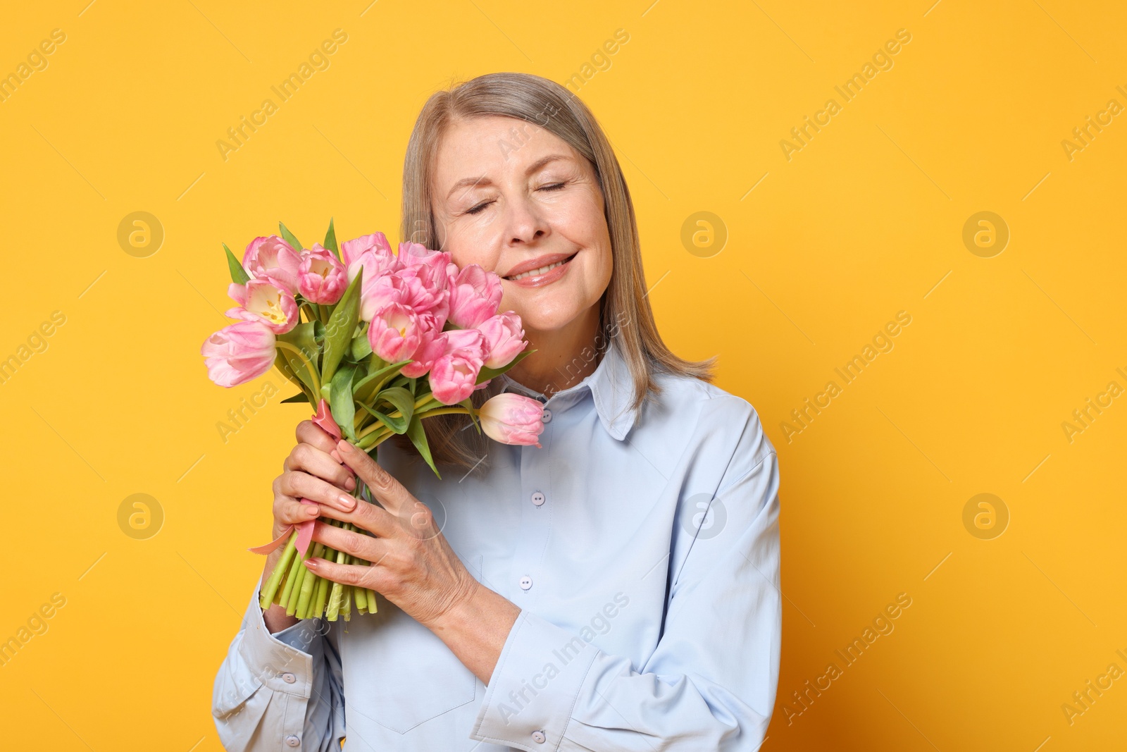 Photo of Smiling woman with bouquet of tulips on yellow background