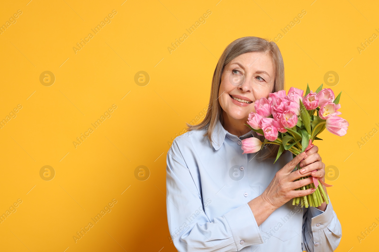 Photo of Smiling woman with bouquet of tulips on yellow background. Space for text