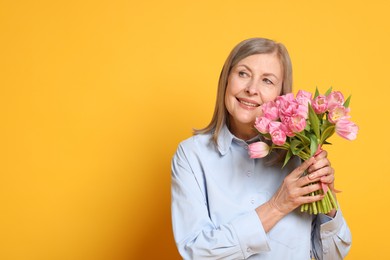 Photo of Smiling woman with bouquet of tulips on yellow background. Space for text