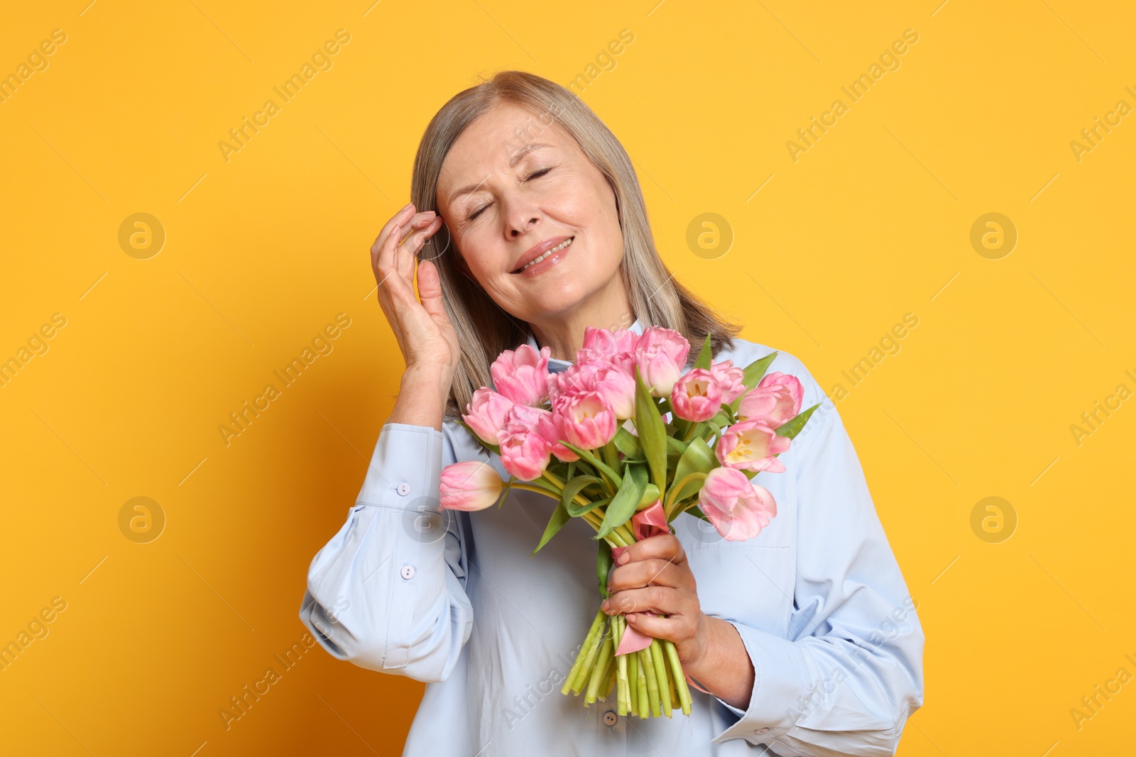 Photo of Smiling woman with bouquet of tulips on yellow background