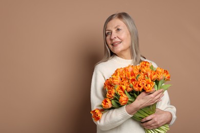 Smiling woman with bouquet of tulips on beige background. Space for text