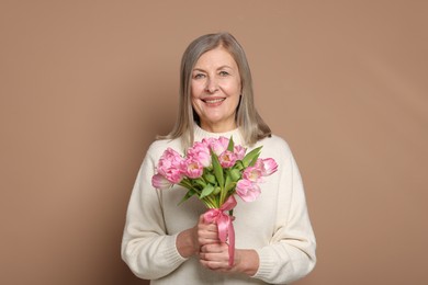 Photo of Smiling woman with bouquet of tulips on beige background